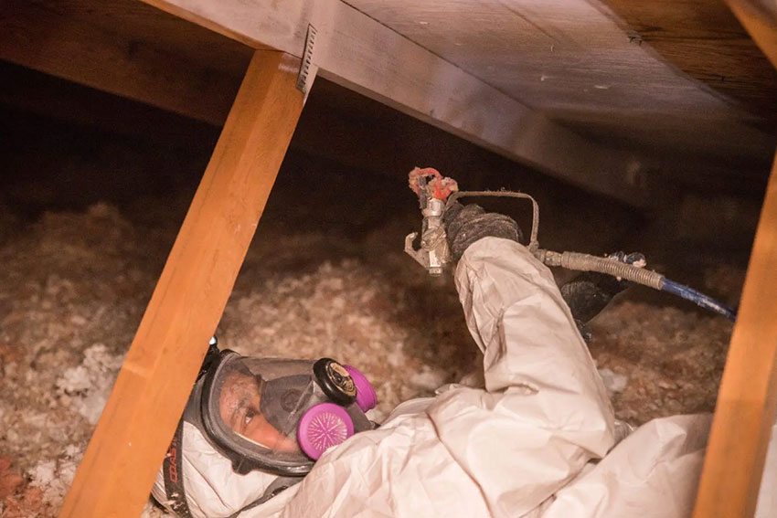 A man in a white coat and mask is engaged in insulation work in a crawl space, part of a Sacramento, CA mold removal service.