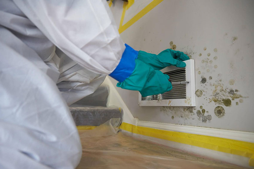 A person wearing a white coat and gloves is cleaning a moldy air conditioner during an HVAC mold removal service in Sacramento, CA.